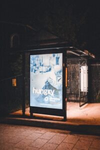 A bus stop at night with an illuminated advertisement display under streetlights.