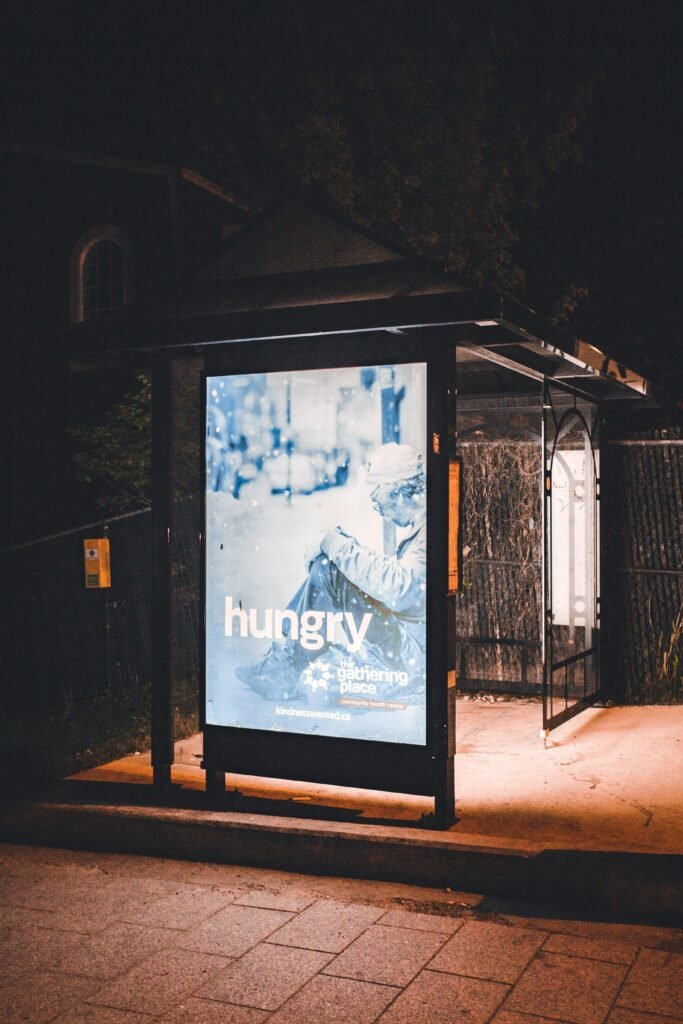 A bus stop at night with an illuminated advertisement display under streetlights.